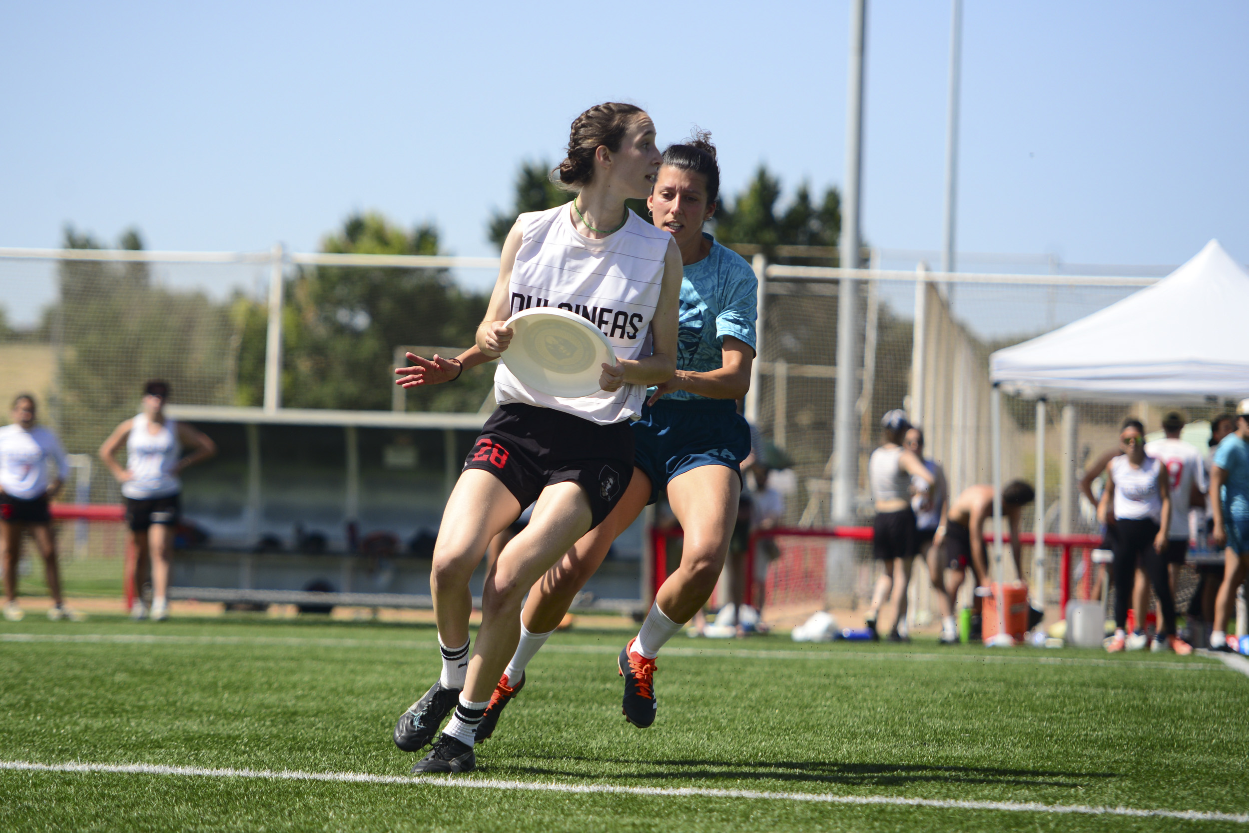 Jugadora de Dulcineas con camiseta blanca protege el disco de una defensora durante un partido de Ultimate Frisbee en césped