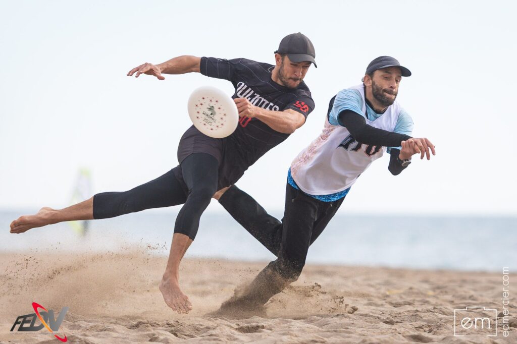 Jugador se lanza en plancha para alcanzar el disco mientras un defensor le presiona en ultimate frisbee playa